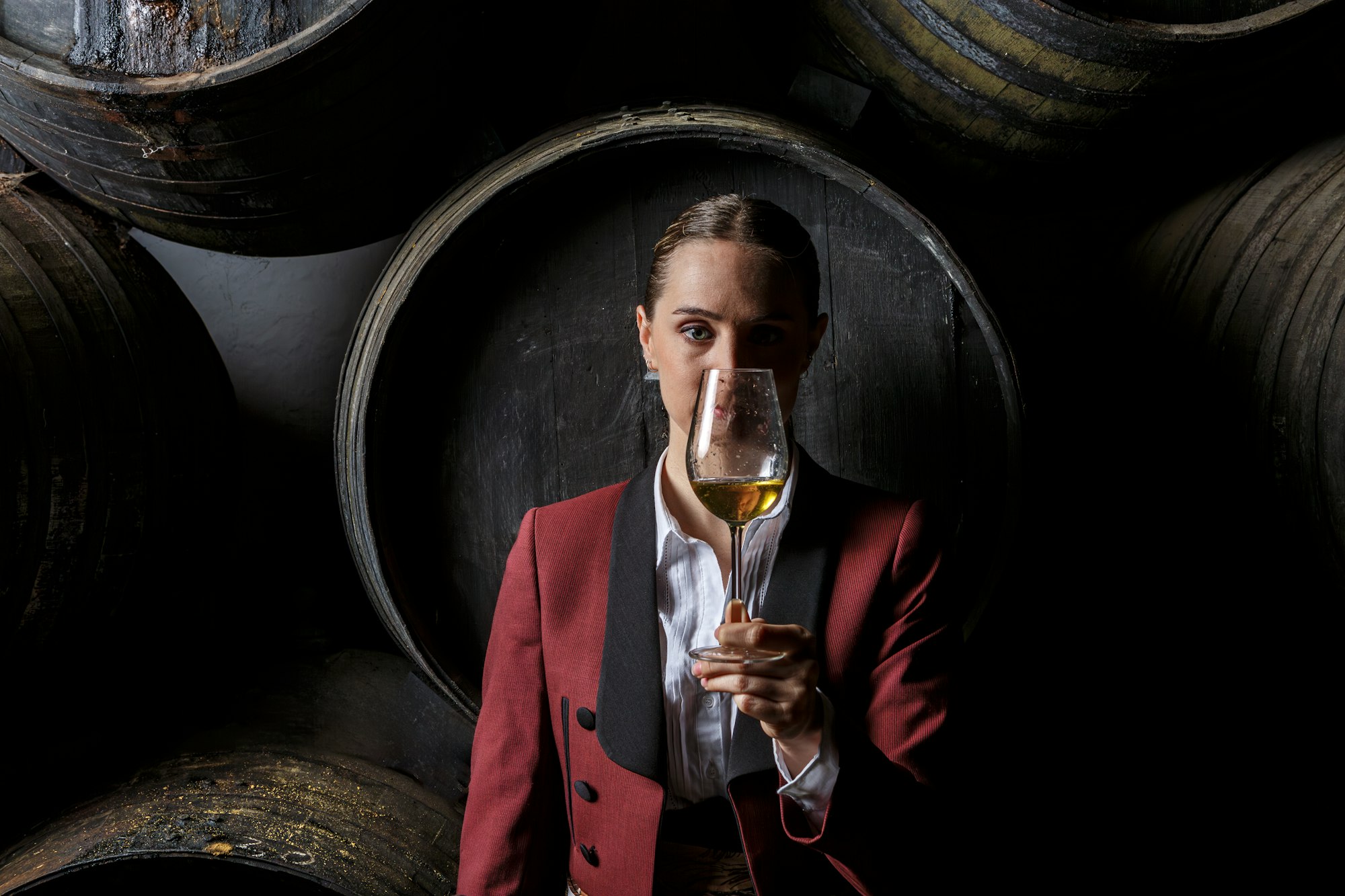 Young woman venenciador demonstrating sample wine in wineglass in cellar